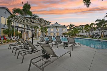 A poolside area with sun loungers and a building in the background. at The Hadley - North Port, FL Apartments, North Port